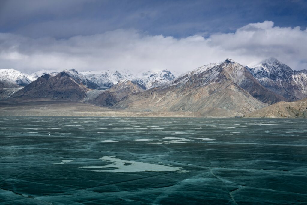 Stunning view of a frozen lake with snow-capped mountains under cloudy skies.